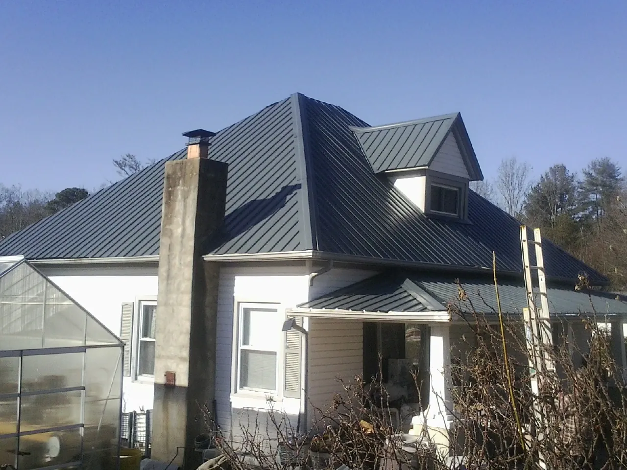 Dark blue standing seam metal roof on a white farmhouse with dormer — Slate & Tile Roof Repair by Roofing Brothers in Jeffersonton
