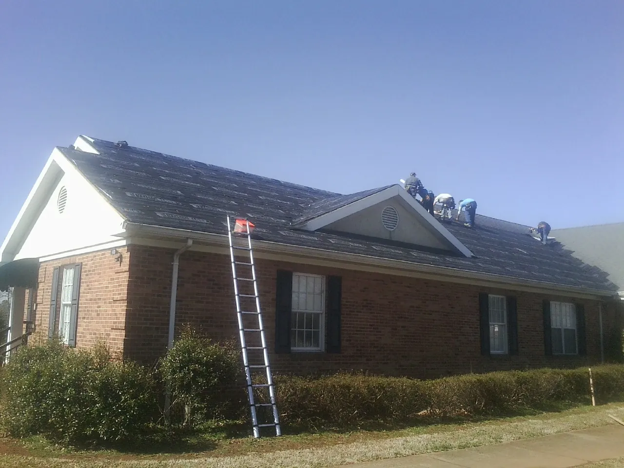 Crew tearing shingles off a brick ranch roof with a ladder set — Emergency Roof Repair work by our crew in Jeffersonton