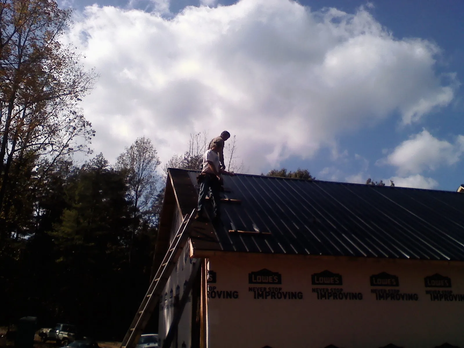 Roofer fastening dark metal panels high against a cloudy sky, from a Roof Inspection job in Jeffersonton
