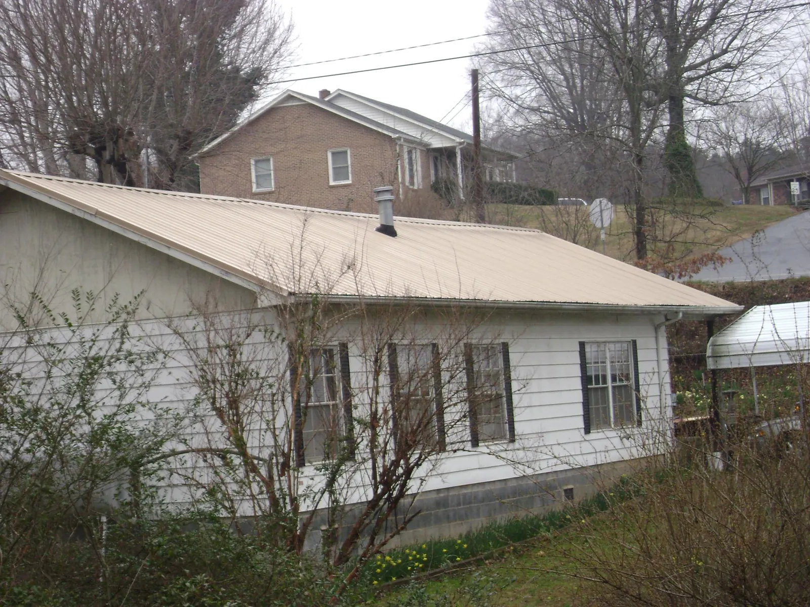 Tan metal roof on a white sided house set into a hillside — Commercial Roofing by Roofing Brothers in Jeffersonton
